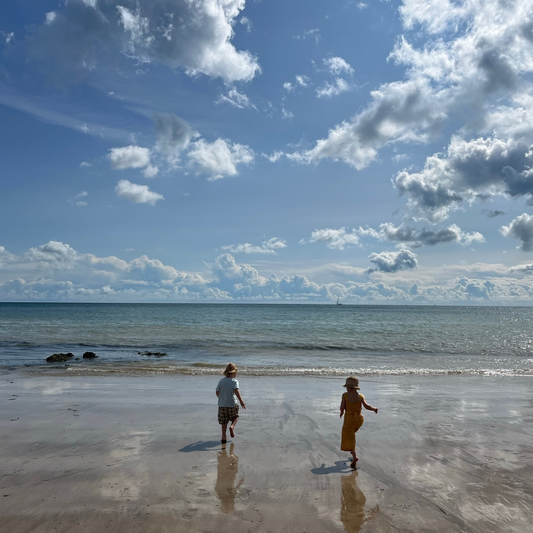Two children run with joy towards the sea at low tide on Stone Bay Beach in Broadstairs, Kent on a sunny day