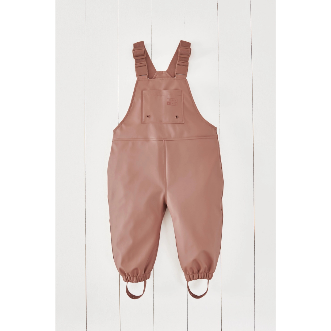 A pair of dusty rose waterproof bib overalls with adjustable shoulder straps and elasticized leg cuffs, displayed flat against a white wood plank background.