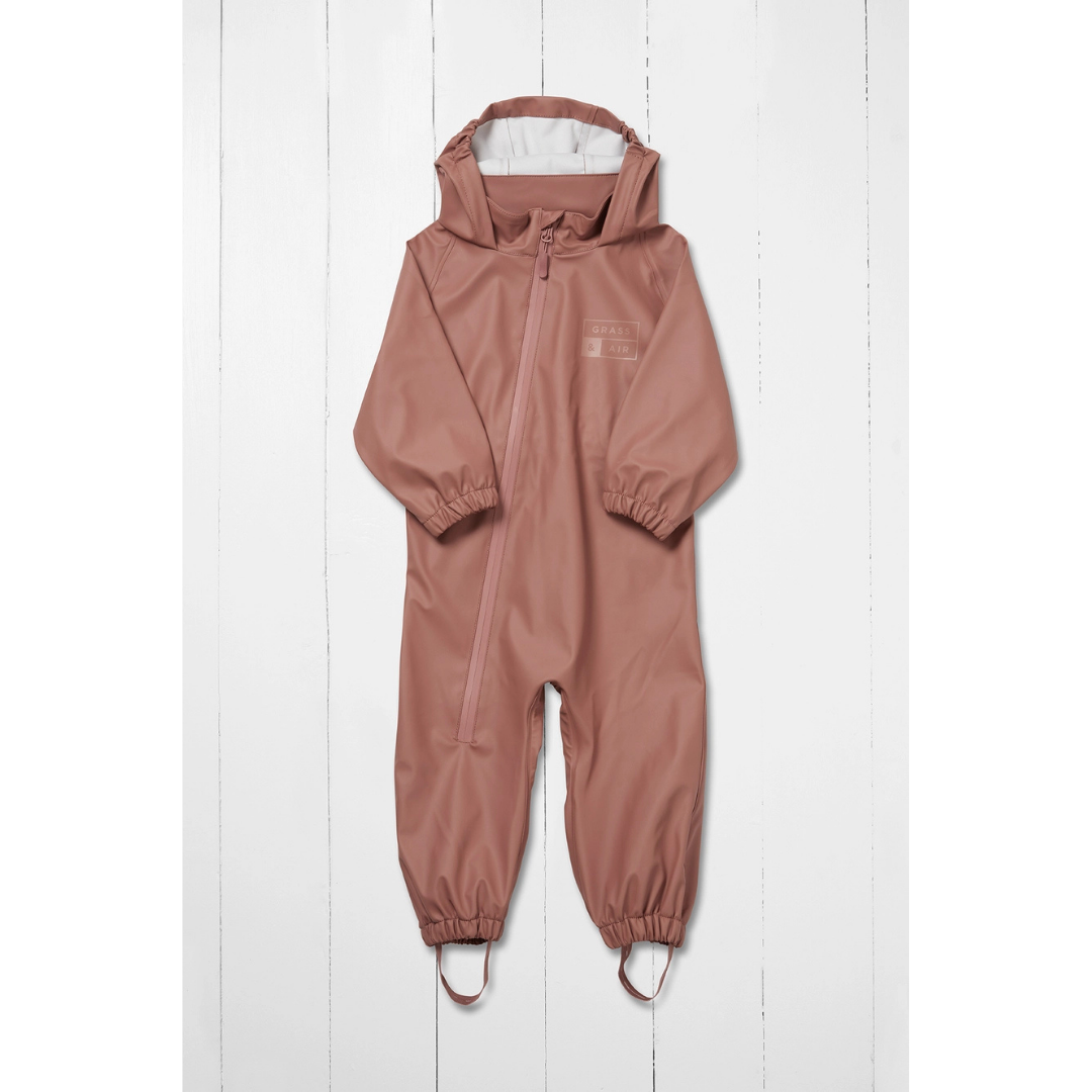 A hooded one-piece kids waterproof puddlesuit in a dusty rose pink color, featuring a front zipper, elastic cuffs, and leg openings, displayed against a white wood plank background.