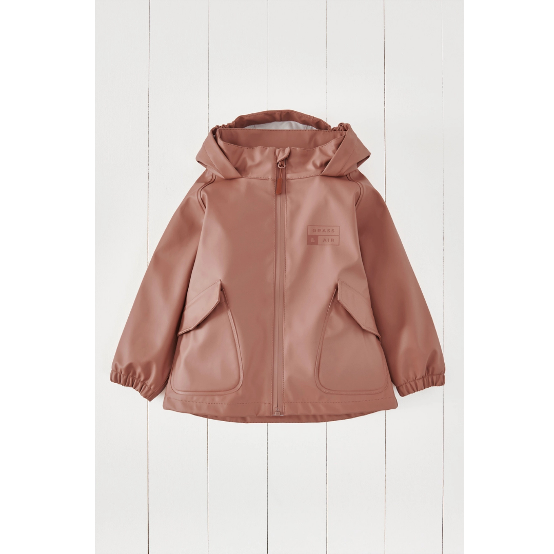 A dusty rose hooded child's rain jacket with front pockets, displayed flat against a white wood panel background.